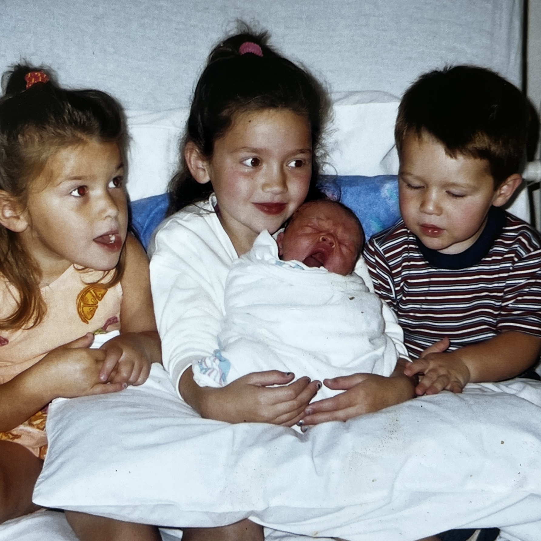 Three siblings on a bed holding a newborn baby